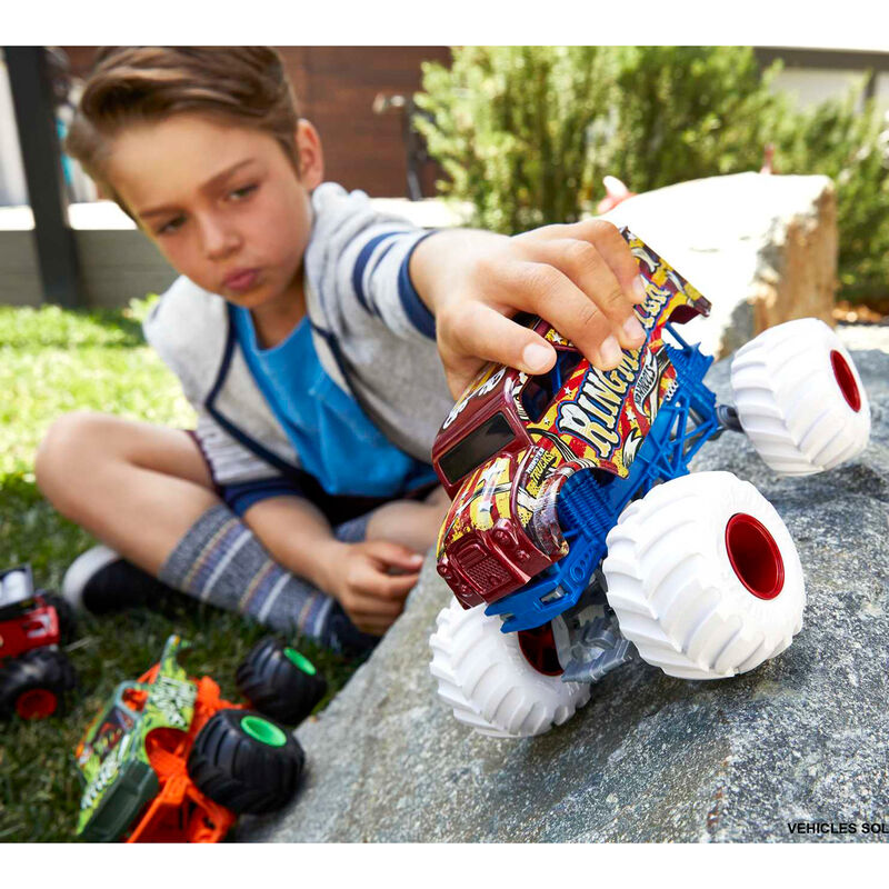 Enfant jouant avec un Hot Wheels Monster Truck sur un terrain accidenté extérieur.