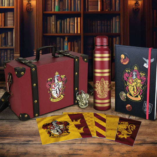 Bouteille en métal aux couleurs Gryffindor et porte-clés assorti posés à côté de la malette sur une surface claire.